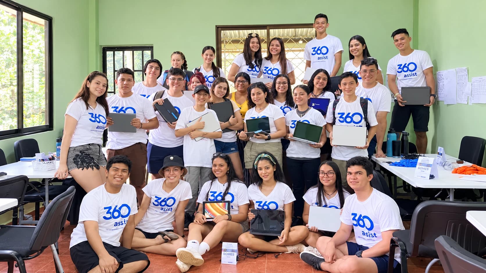 360Assist volunteers and students in 360Assist shirts holding donated laptops